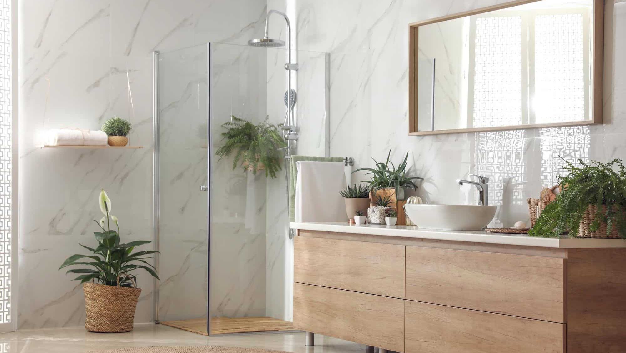 Moderne baderom med lyse flater, grønne planter og dusj med glassvegg.