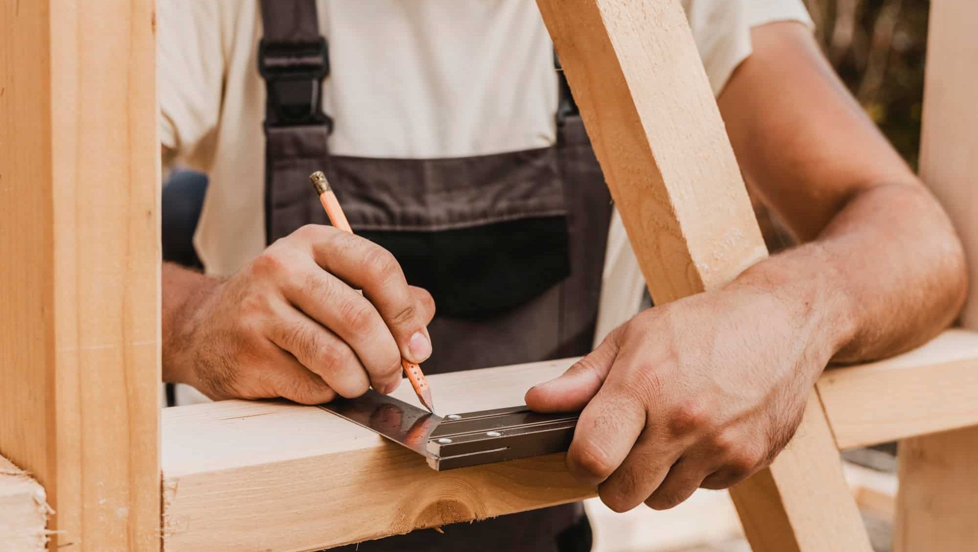 Håndverker som markerer målinger på treverk ved hjelp av blyant og vinkelhake.
